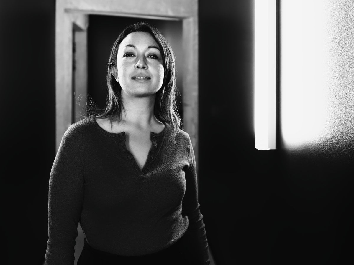 Black and white portrait of a woman standing in a hallway, illuminated by a bright vertical light source on the right.
