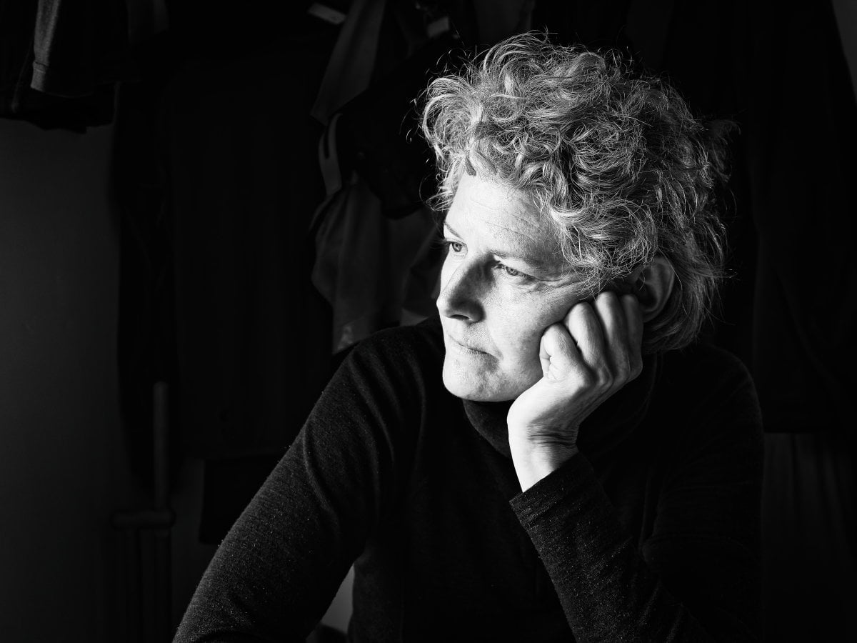 Black and white portrait of a woman with curly hair resting her cheek on her hand and looking to the side against a dark background.